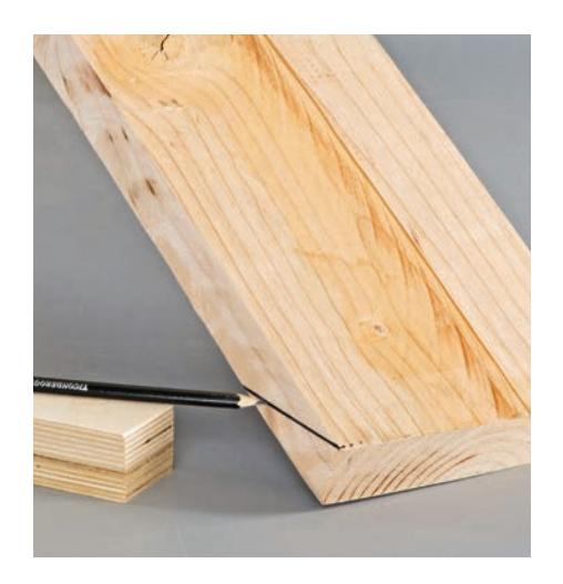 Tracing a cutting line along the bottom of a chair leg using scrap wood as a guide.