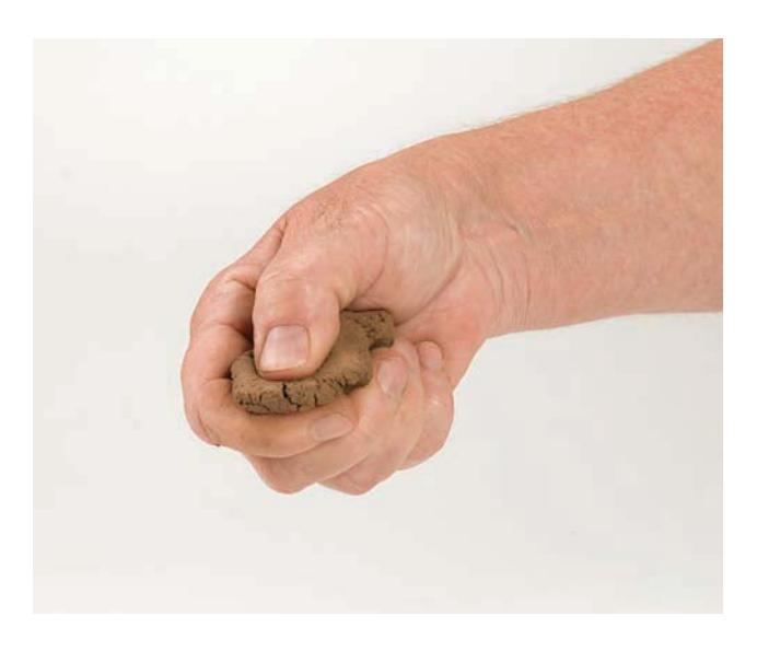 A hand pressing a soil ball between thumb and forefinger to form a ribbon